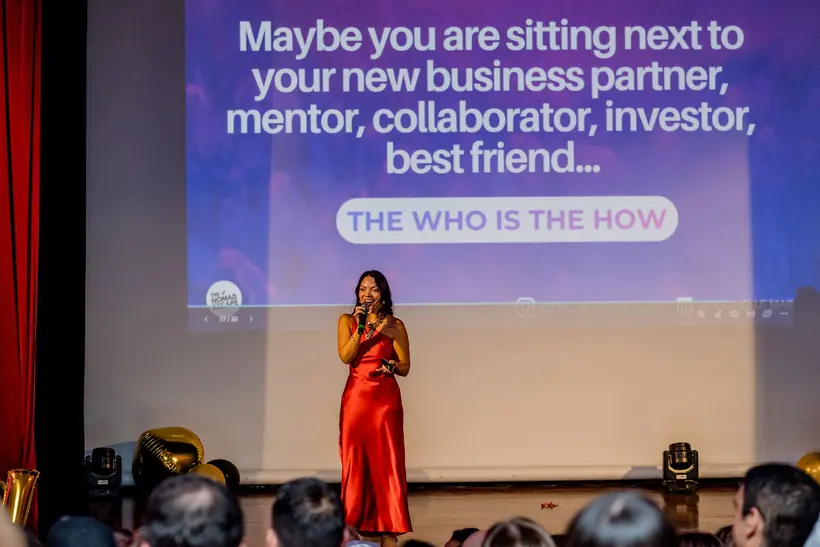 Michelle on stage in front of a slide reading: maybe you are sitting next to your new business partner, mentor, collaborator, investor, best friend
